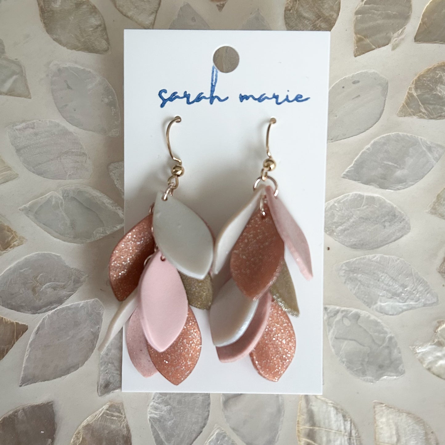 Pair of pink and rose gold earrings on a 'sarah marie' branded card against a textured background