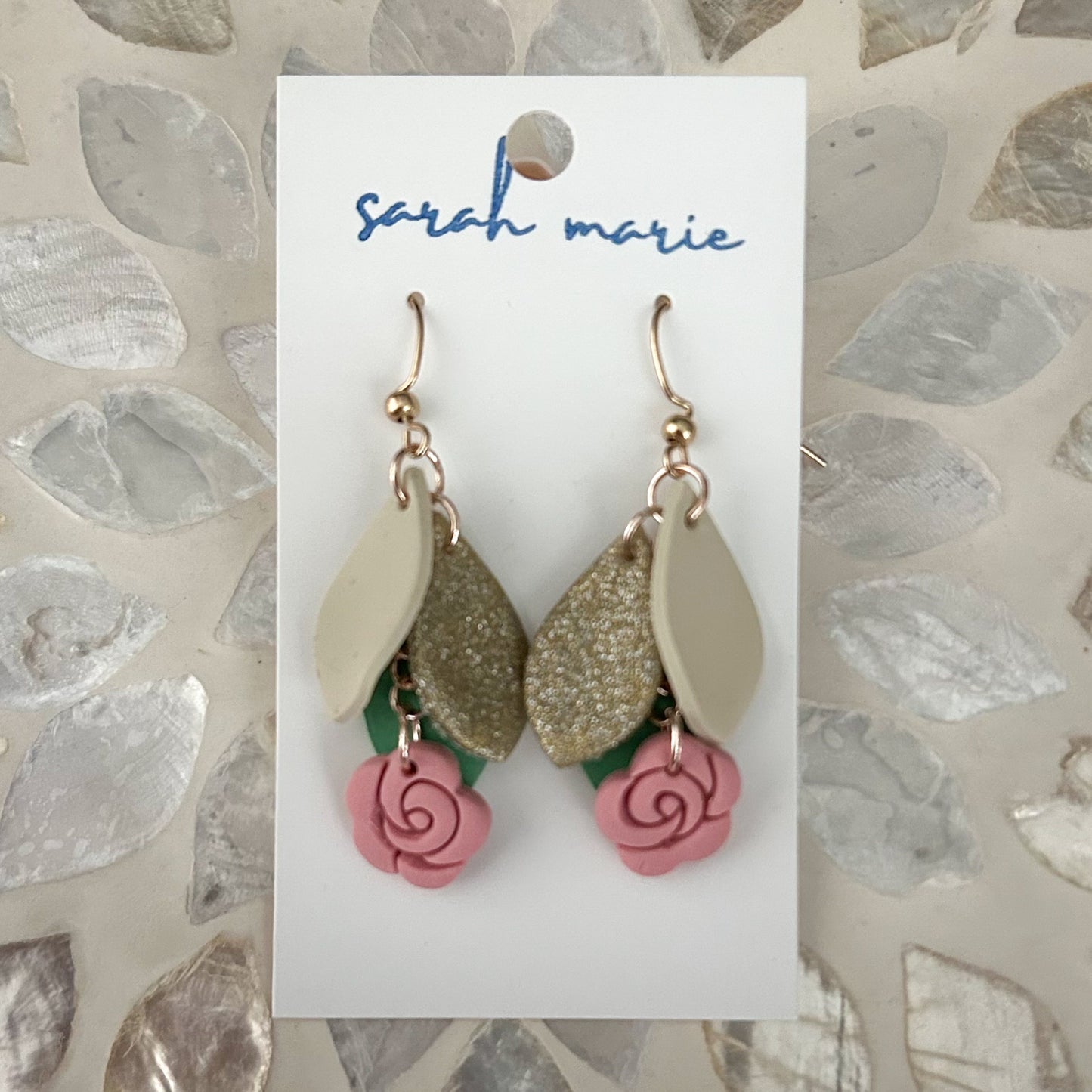 Pink gold and green earrings on a 'sarah marie' branded card with a textured stone background