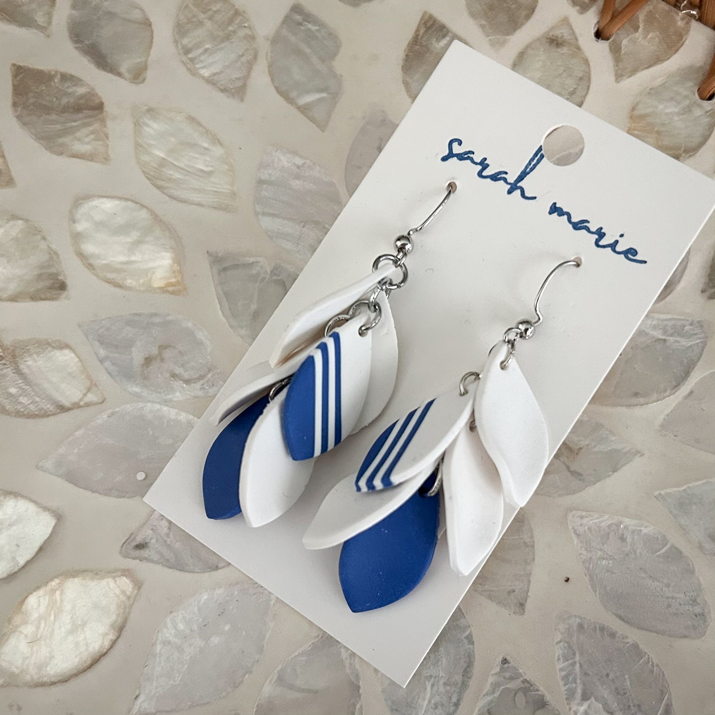 Pair of blue and white dangle hook earrings on a 'Sarah Marie' branded card against a textured stone background