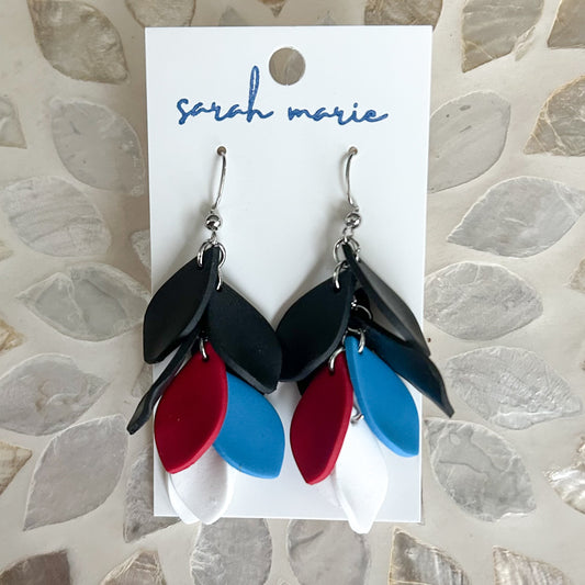 Red blue black and white leaf-shaped dangle hook earrings on a 'sarah marie' branded card against a stone background