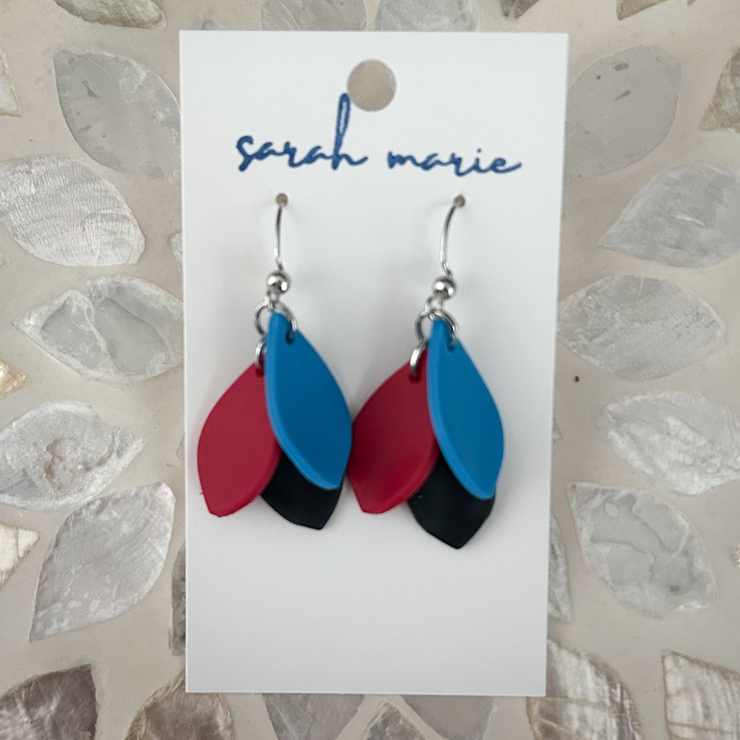 Red blue and black leaf-shaped earrings on a 'sarah marie' branded card against a textured background.