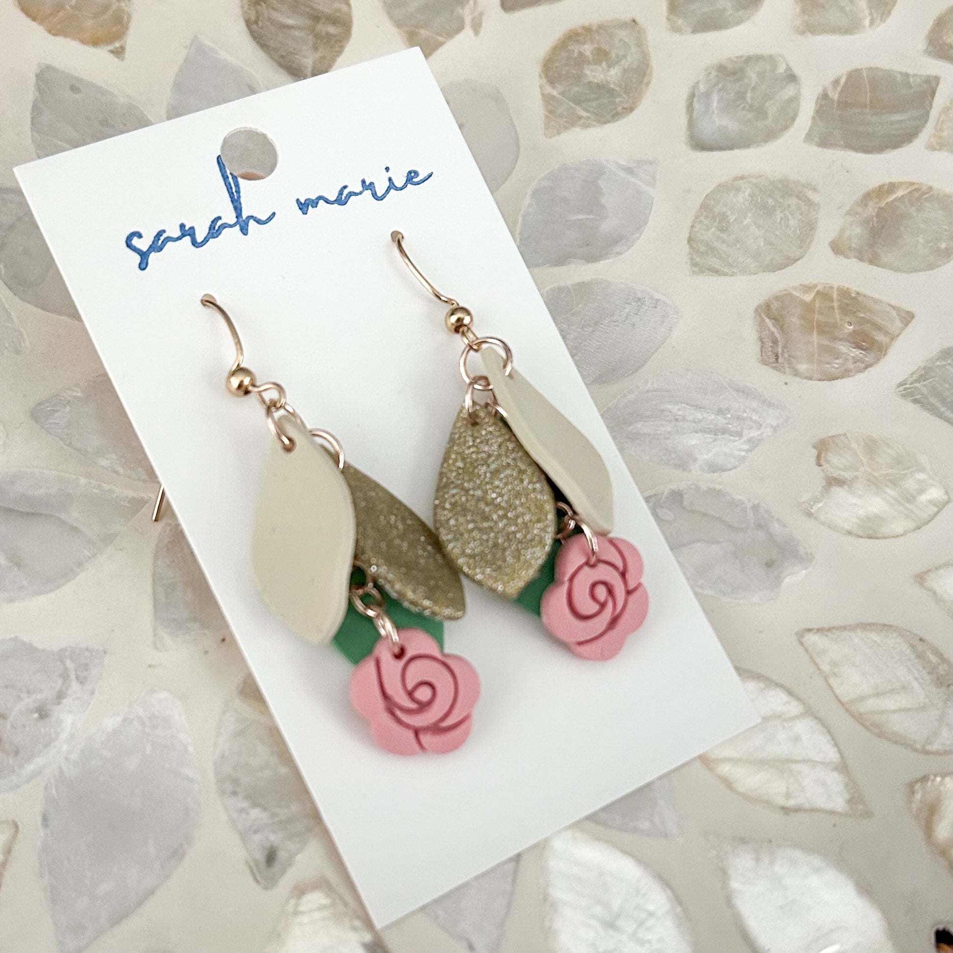 Earrings with gold, ivory, and pink elements on a 'Sarah Marie' branded card.