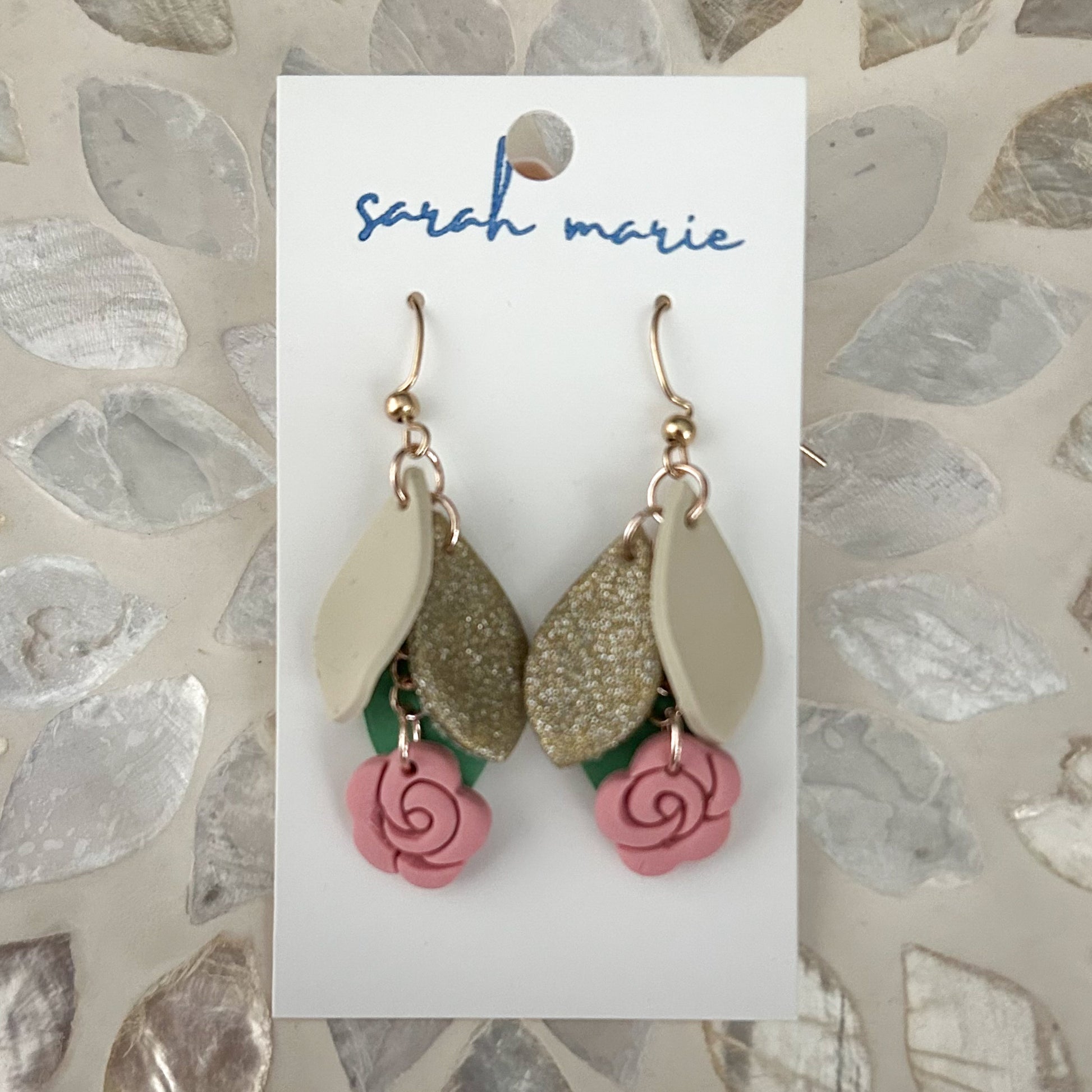 Pink gold and green earrings on a 'sarah marie' branded card with a textured stone background
