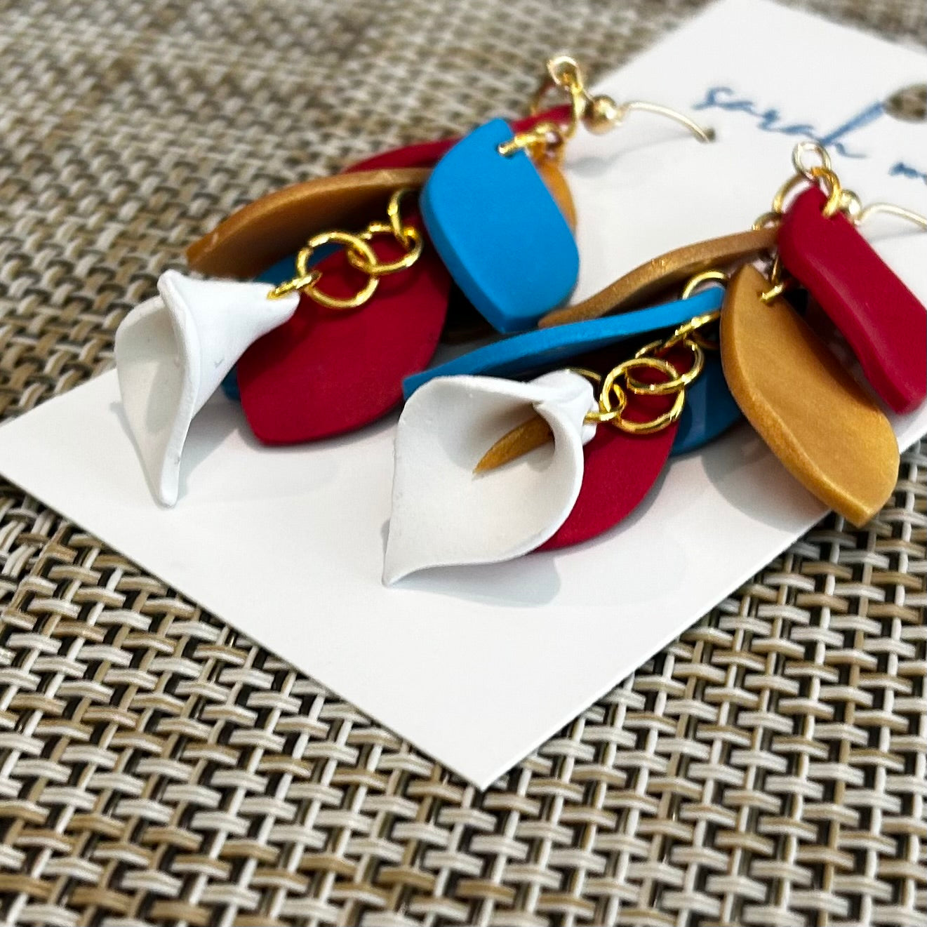 Colorful leaf shaped dangles with a white calla lily earrings on a white card with a textured surface background