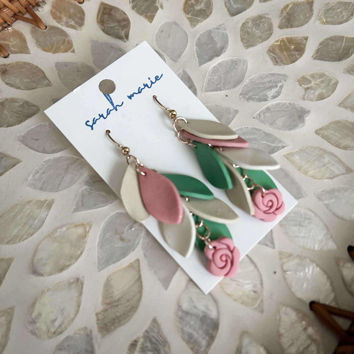 Pink, green and ivory Leaf-shaped earrings on a 'Sarah Marie' branded card against a textured stone background