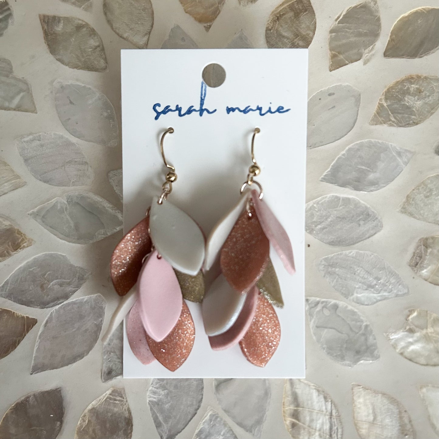 Pink, rose gold & gold dangle hook earrings on a card with 'sarah marie' branding against a stone-patterned background