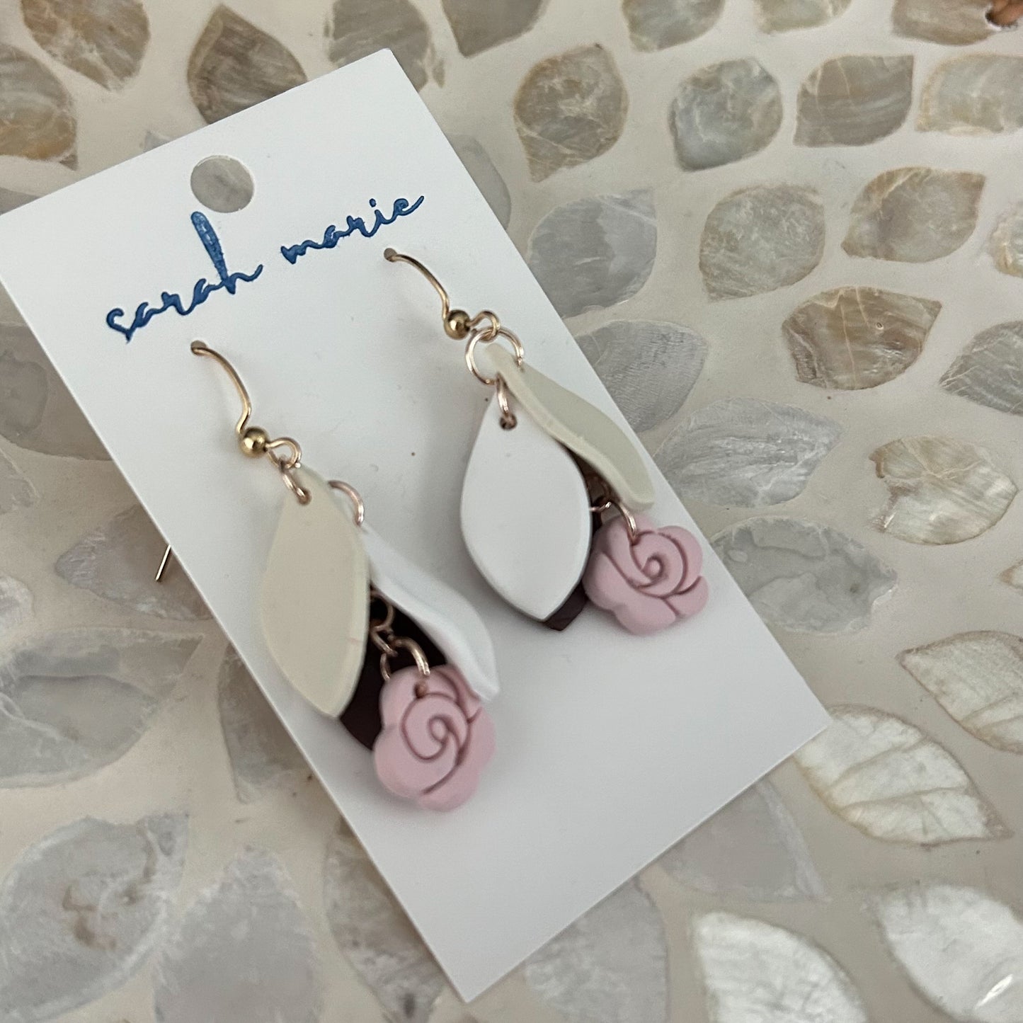 Pair of earrings with pink floral charms on a 'sarah marie' branded card.