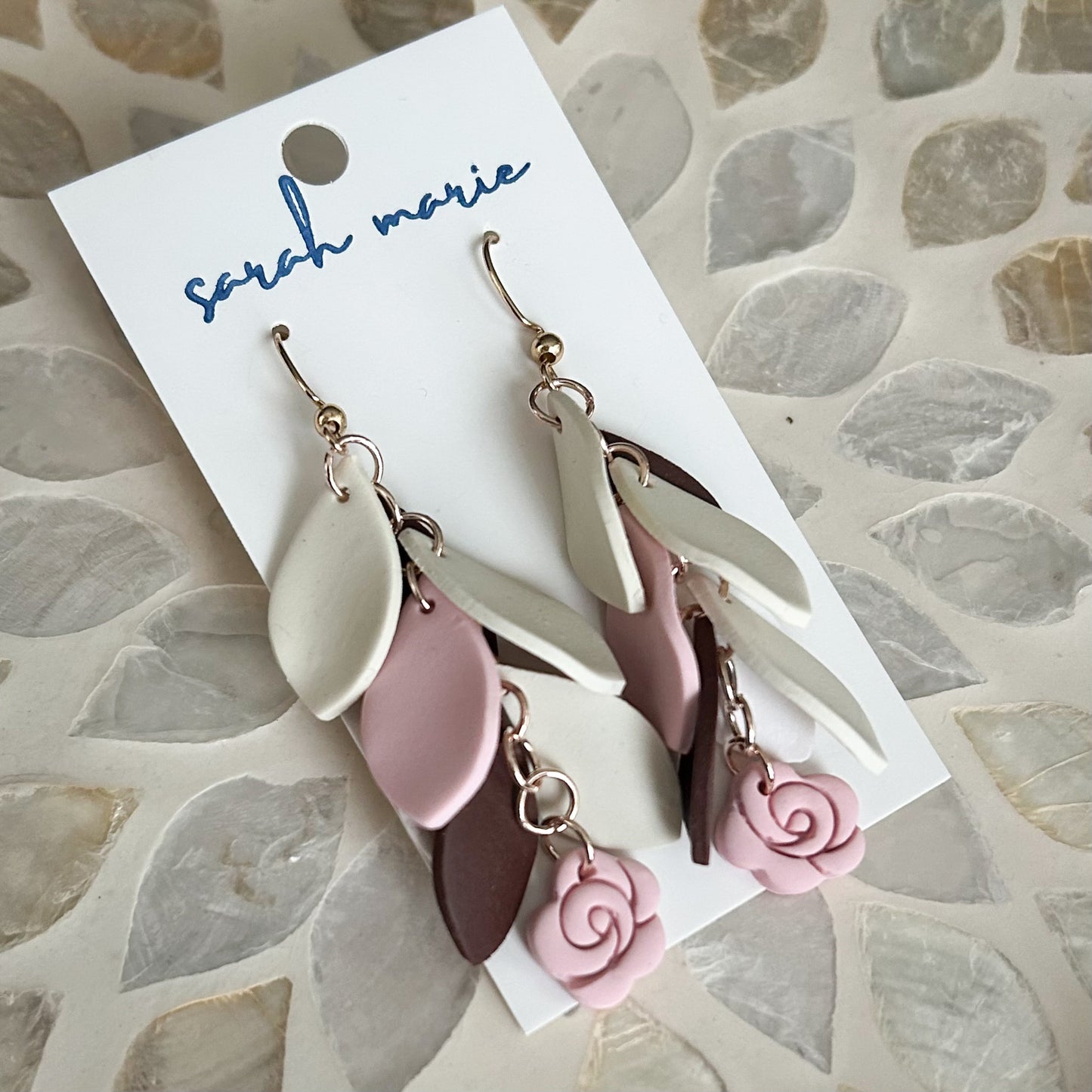 Pair of pink brown and ivory earrings on a 'sarah marie' branded card against a stone-patterned background