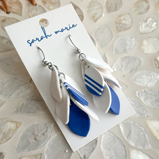 Pair of blue and white dangle hook earrings on a 'Sarah Marie' branded card against a textured stone background.