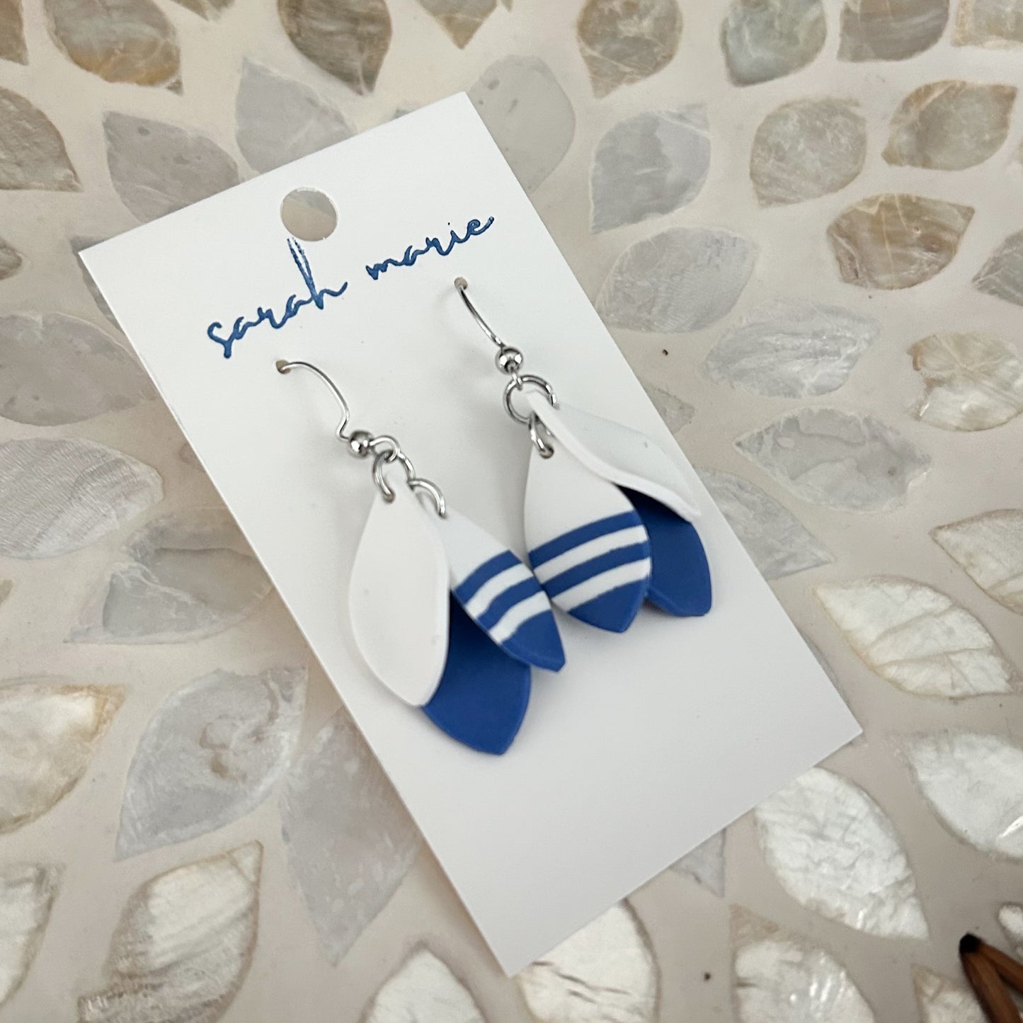Pair of blue and white 1.5” dangle hook earrings on a 'sarah marie' branded card against a textured stone background